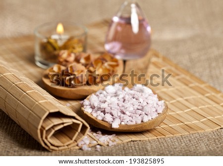 Spa background with sea salt in wooden spoon, dried flowers, candle and essential oil on the mat.