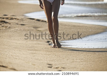 Young woman walking alone on the sand beach in the sunset and leave footprints behind.