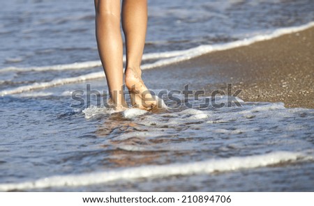 Young woman walking alone on the sand beach in the sunset and the water is lapping at her feet.