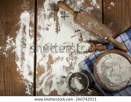 Flour and kitchen utensils on wooden background.