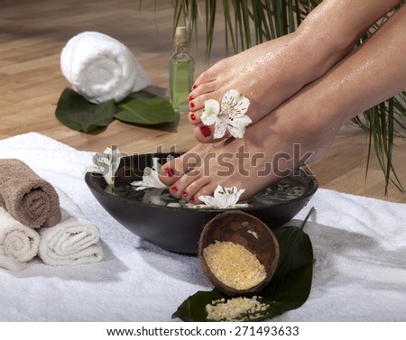 Female feet with drops of water soaked in spa bowl with flowers and rocks.