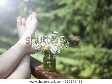 Bunch of beautiful camomile flowers and human feet on green bokeh background.