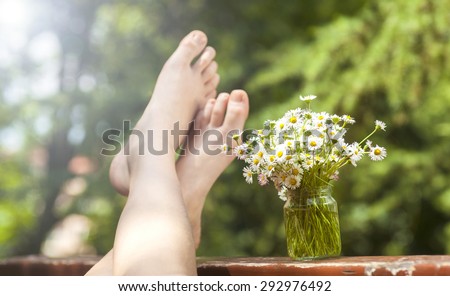 Bunch of beautiful camomile flowers and human feet on green bokeh background.