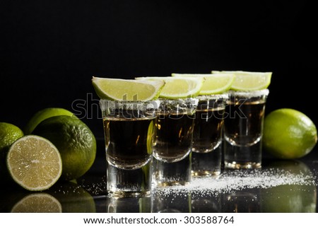 Gold tequila shot with lime fruits on black background