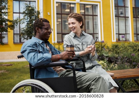Cheerful beautful woman sitting on bench and sharing funny video with disabled biyfriend during stroll Photo stock © 