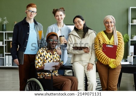 Portrait of diverse creative team looking at camera with cheerful smiles while posing in office, wheelchair user inclusion Foto stock © 