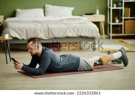 Side view portrait of man with prosthetic leg laying on floor at home and using smartphone Foto stock © 