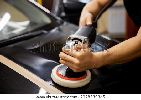 The concept of detailing and polishing cars. The hands of a professional car service worker, with an orbital polisher, polish the black luxury hood of a car in an auto repair shop. car polishing