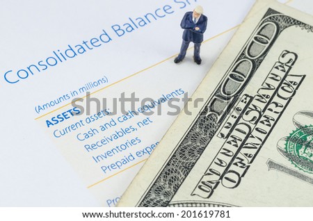 miniature businessman standing with US dollar banknote on the balance sheet