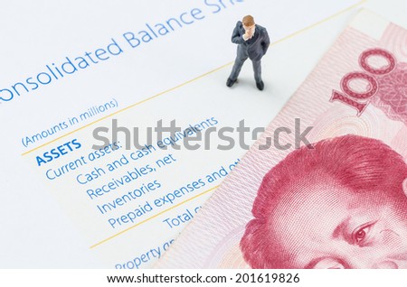 miniature businessman standing with Chinese banknote on the balance sheet