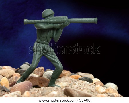 Green army man standing on rocks and sand in front of a studio background.