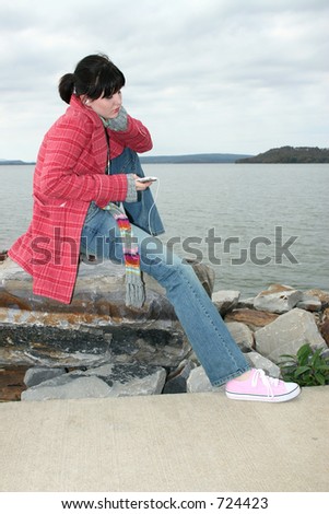 Beautiful young woman sitting on rock by the lake listening to digital music on headphones.
