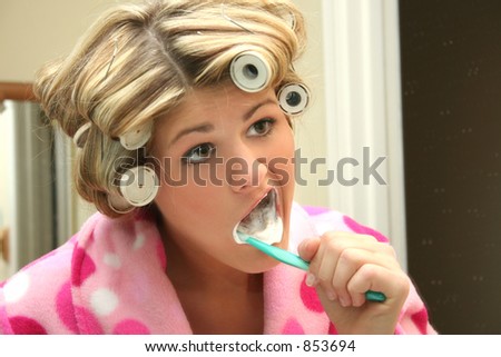 Beautiful blonde woman brushing teeth in bath robe and hair rollers.
