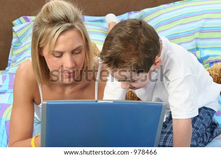 Mother and son in pajamas in bed working on laptop together.  Ages 29 and 5.