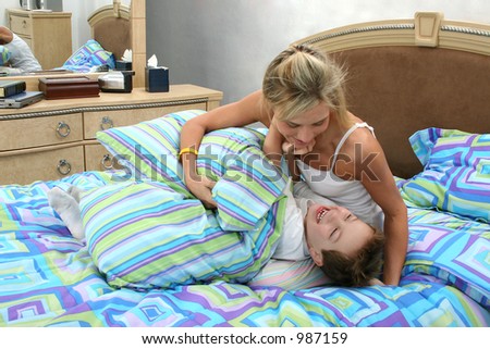 Mom and son having tickle fight at home in bed.