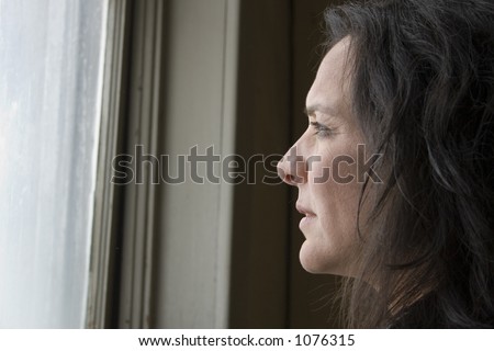 Thirty-eight year old impoverished woman looking out window of low income home.