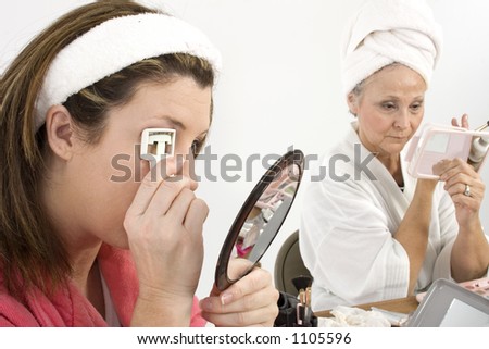 Two woman doing facials and make-overs. Focus on woman on left curling eyelashes.