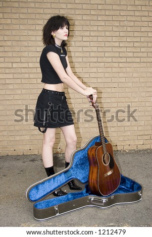 Beautiful young guitarist taking a break.   Standing outside with acoustic guitar.