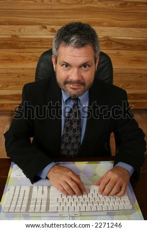 Fourty something business man in suit sitting at desk typing on keyboard.