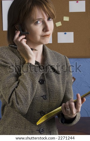 Thirty something year old woman in office taking notes wearing wireless communication piece in ear.