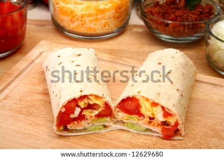 Breakfast burrito in kitchen or restaurant.  Eggs, cheese, tomato, lettuce, onion, chipotle, bacon.