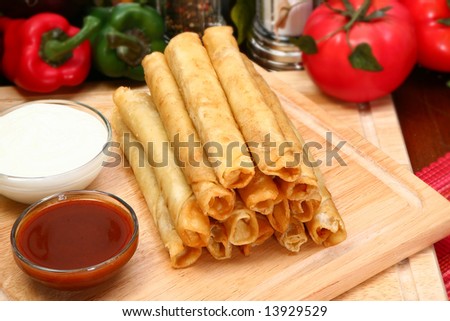 Stack of chicken taquitos with hot sauce and sour cream in kitchen or restaurant