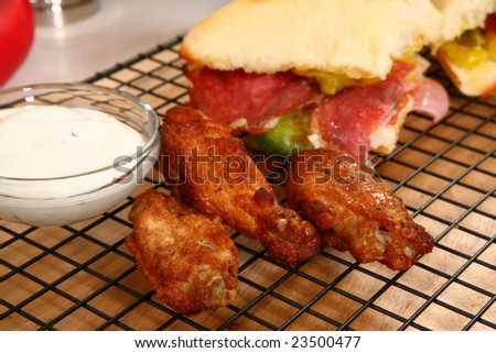 Hot spicy buffalo style chicken wings in front of bowl of Blue Cheese dressing and deli sandwich.