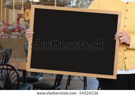 Woman holding blank chalkboard in front of carousel restaurant area.
