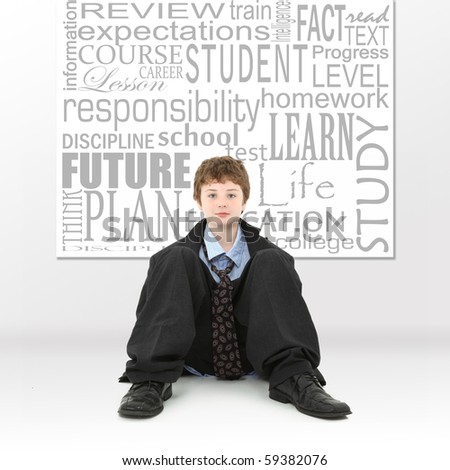 Attractive ten year old american boy in big baggy sit sitting in front of educational themed words hanging on wall.