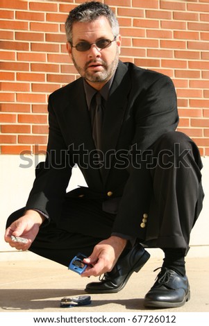 Attractive 40 year old business man picking up broken cellphone from sidewalk.