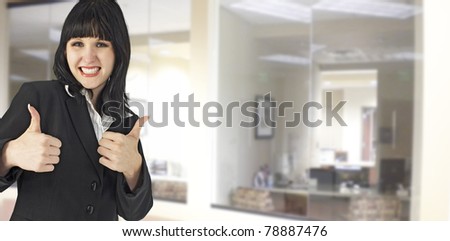 Attractive young woman in suit giving two thumbs up at office with clipping path.