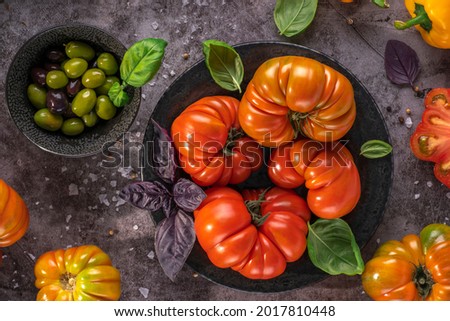 Whole and sliced organic tomatoes Raf Coeur De Boeuf. Raw fresh tomatos with sea salt and basil and olives in plates on rustic dark metal texture background Zdjęcia stock © 