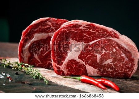 Raw rib eye beef steak with pepper and herbs on a wooden background in a butcher shop