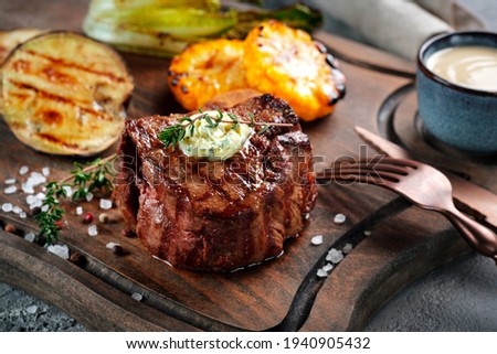 Grilled beef tenderloin steak on a wooden board with butter and thyme. Filet Mignon recipe with vegetables
