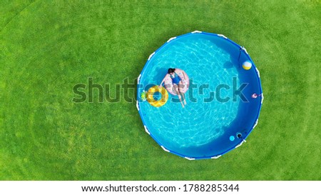 Aerial. Girl swims in a metal frame pool with inflatable toys. Frame pool stand on a green grass lawn. Top view. Copy space.
