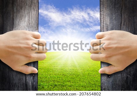 Two hands opening old wooden door to the new world. New life concept.