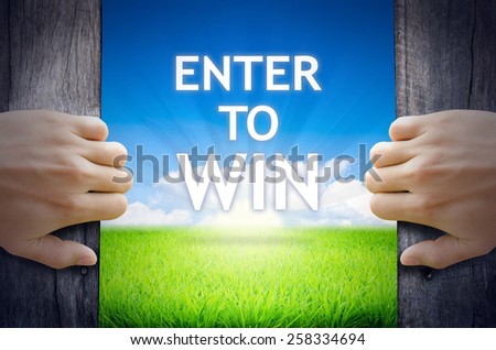 Enter to WIN. Hand opening an old wooden door and found Enter to WIN word floating over green field and bright blue Sky Sunrise.