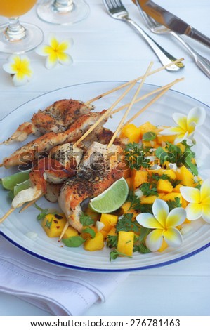 chicken skewers and mango salsa on a white round plate and white wooden background.