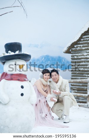 The bride and groom play in the snow, the snow beside a snowman