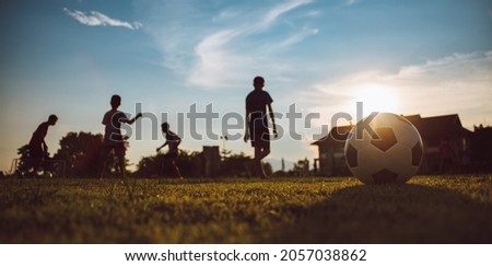 Silhouette action sport outdoors of a group of kids having fun playing soccer football under the twilight sunset. 商業照片 © 