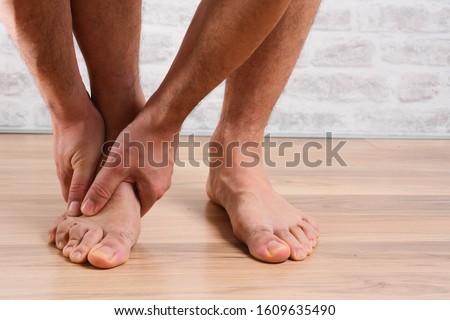 Pain in the foot, man holds hands to his feet, foot massage, cramp, muscular spasm, red accent on the foot, close-up Stock fotó © 