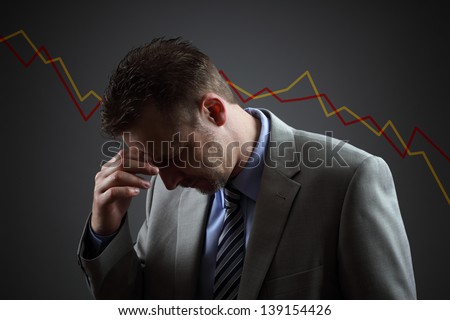 Depressed businessman in economic crisis with line graph showing negative trend