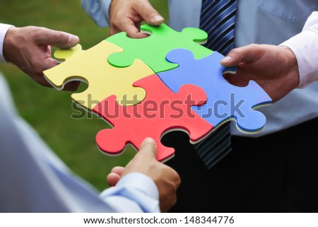Teamwork concept four business people holding jigsaw puzzle pieces together