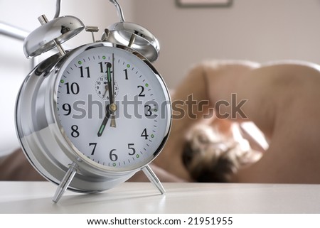 Alarm clock on bedside table with man sleeping in bed