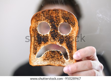 Man holding up a burnt slice of toast with an unhappy smiley concept for bad start to the day