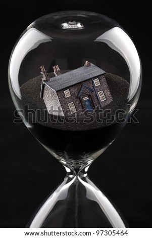 hourglass with house sinking into sand concept for housing market recession or housing difficulties