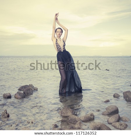 Glamorous lady in an gorgeous dress standing in sea