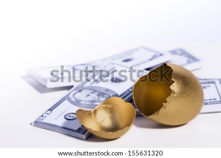 A golden egg cracked open sits in front of some money.