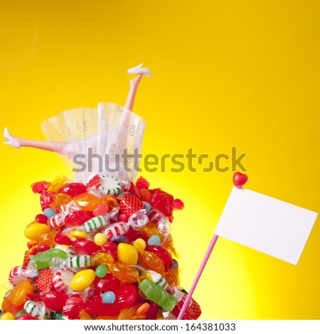 Legs from a generic children doll stick out of a pile of candy against a yellow background.