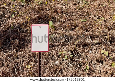 A blank sign against an embankment of vegetation.